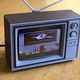 A tiny 3D-printed Toshiba TV with a modern LCD screen playing Commander Keen on a wooden table.